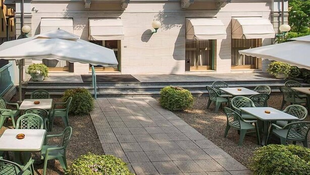 A hotel courtyard with outdoor seating, covered by umbrellas, and flower boxes on the windowsills.