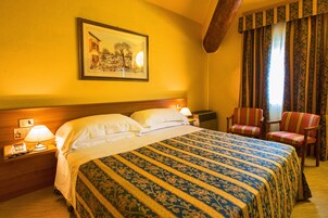 Habitación de hotel con una cama grande, una mesita de noche con lámpara, una silla y un cuadro en la pared.
