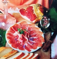 Una tabla de embutidos con diferentes carnes, pan y un vaso de agua.