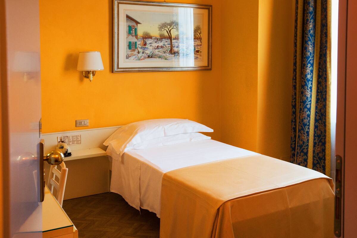 A hotel room with a bed, a nightstand, a lamp, and a painting on the wall.