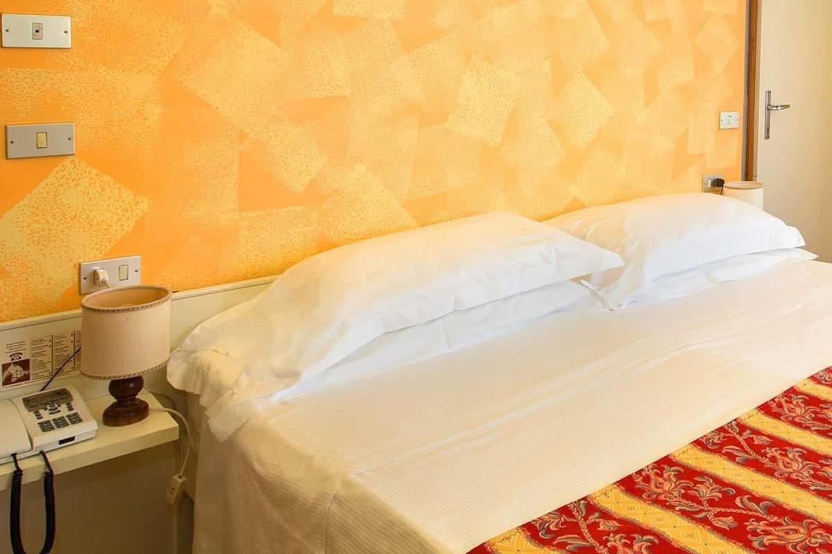 A hotel room with a bed, a telephone, and a wall with a geometric pattern.