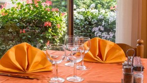 A table set with wine glasses and a knife, with a wooden chair and a window view of greenery.