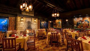 Un restaurante con varias mesas y sillas, una chimenea de piedra y obras de arte en las paredes.