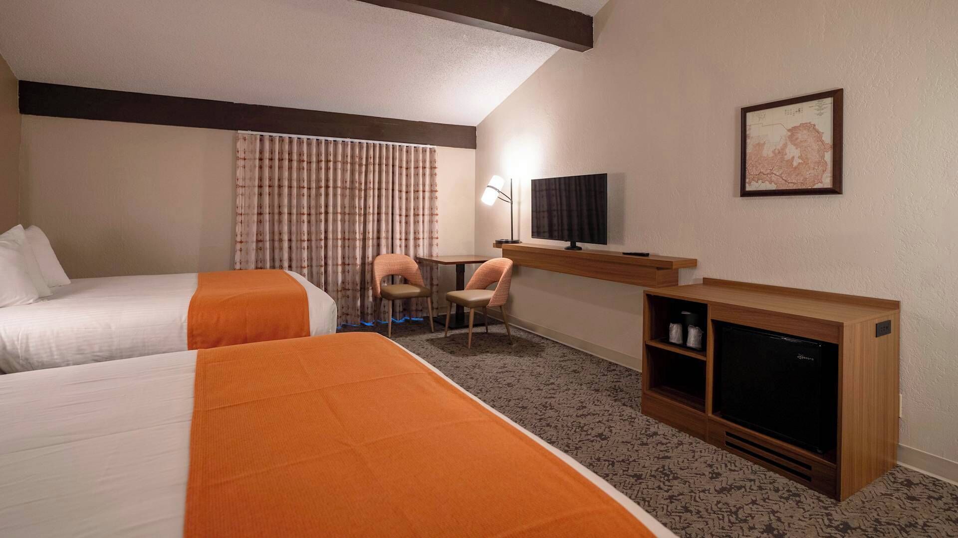 Una habitació d'hotel amb dos llits, un escriptori amb una cadira, una televisió i una llar de foc.