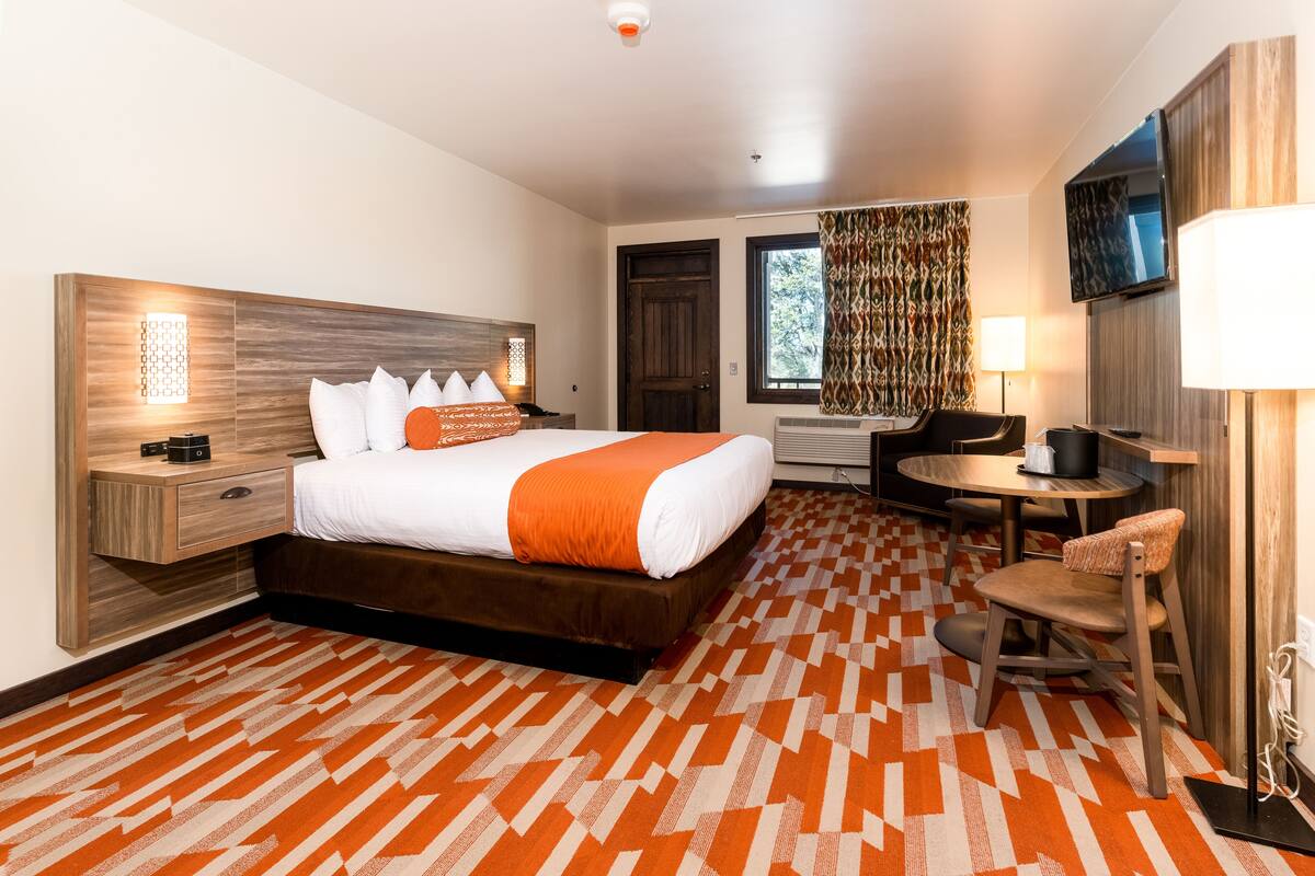 Ein Hotelzimmer mit einem großen Bett, einem Schreibtisch, einem Sessel, einem Fernseher und einem gemusterten Teppich.