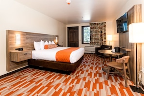 A hotel room with a large bed, a desk, a chair, a TV, and a patterned carpet.