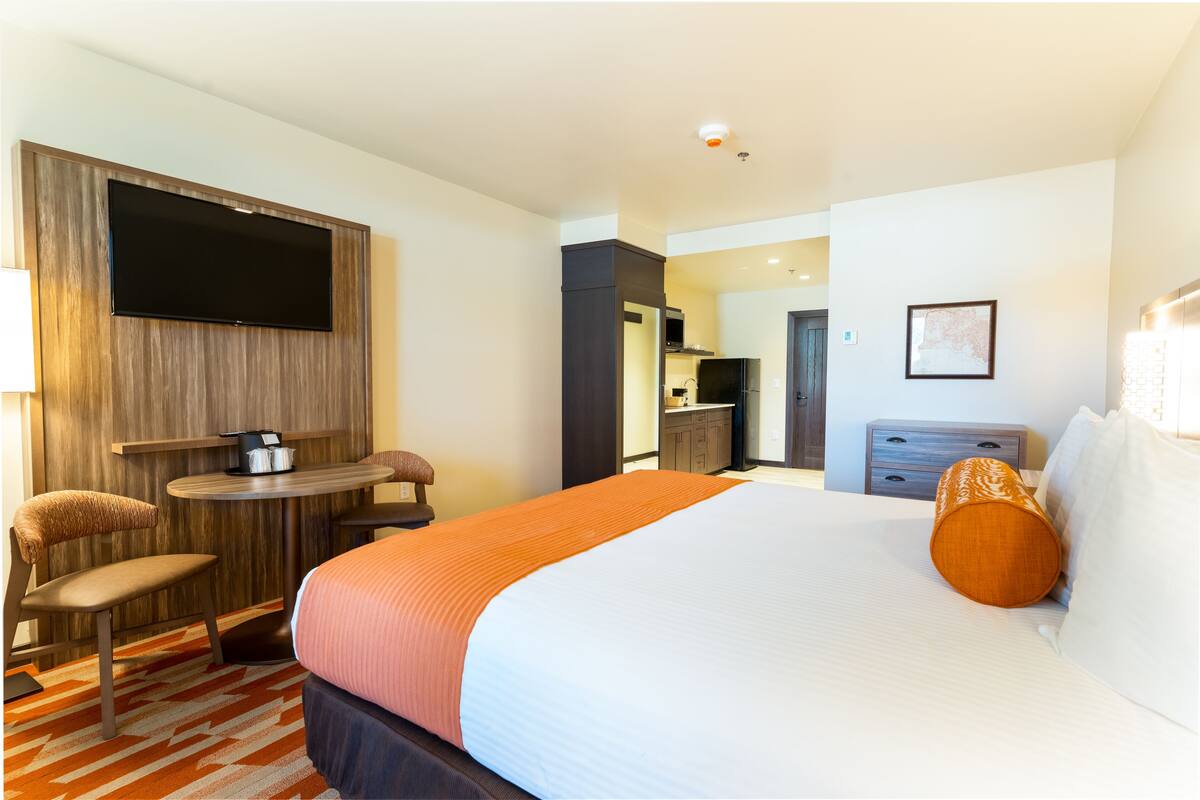 Ein Hotelzimmer mit Bett, Schreibtisch, Stuhl, Fernseher, einem kleinen Tisch und einer Küchenzeile.