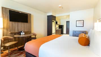 A hotel room with a bed, a desk, a chair, a TV, a small table, and a kitchenette.