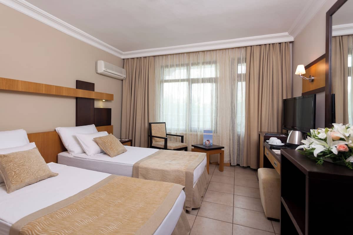 Ein Hotelzimmer mit zwei Betten, einem Schreibtisch mit Fernseher und einem Sessel.