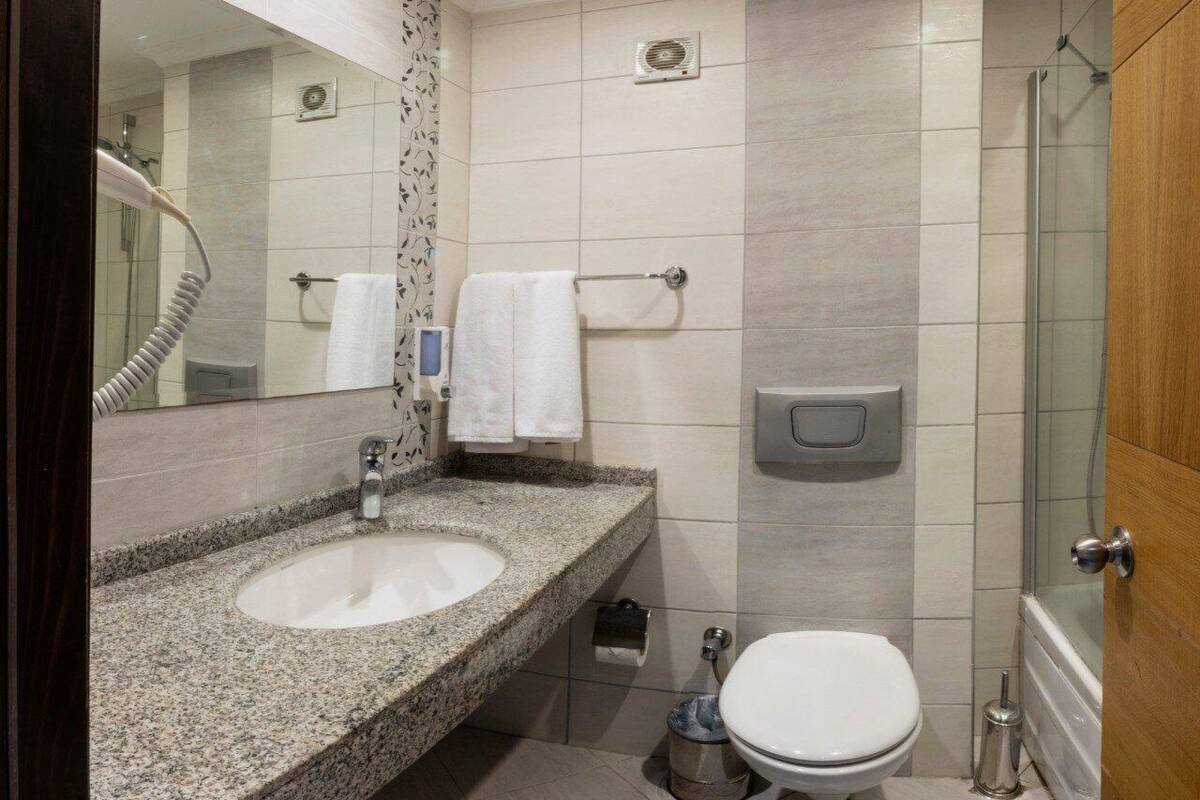 A modern bathroom with a granite sink, a toilet, a shower, and a towel rack.