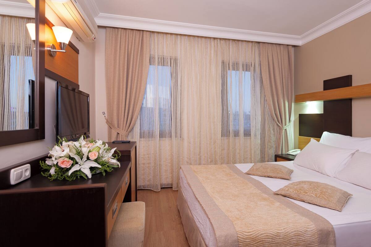 A hotel room with a bed, bedside table, lamp, curtains, and a mirror.
