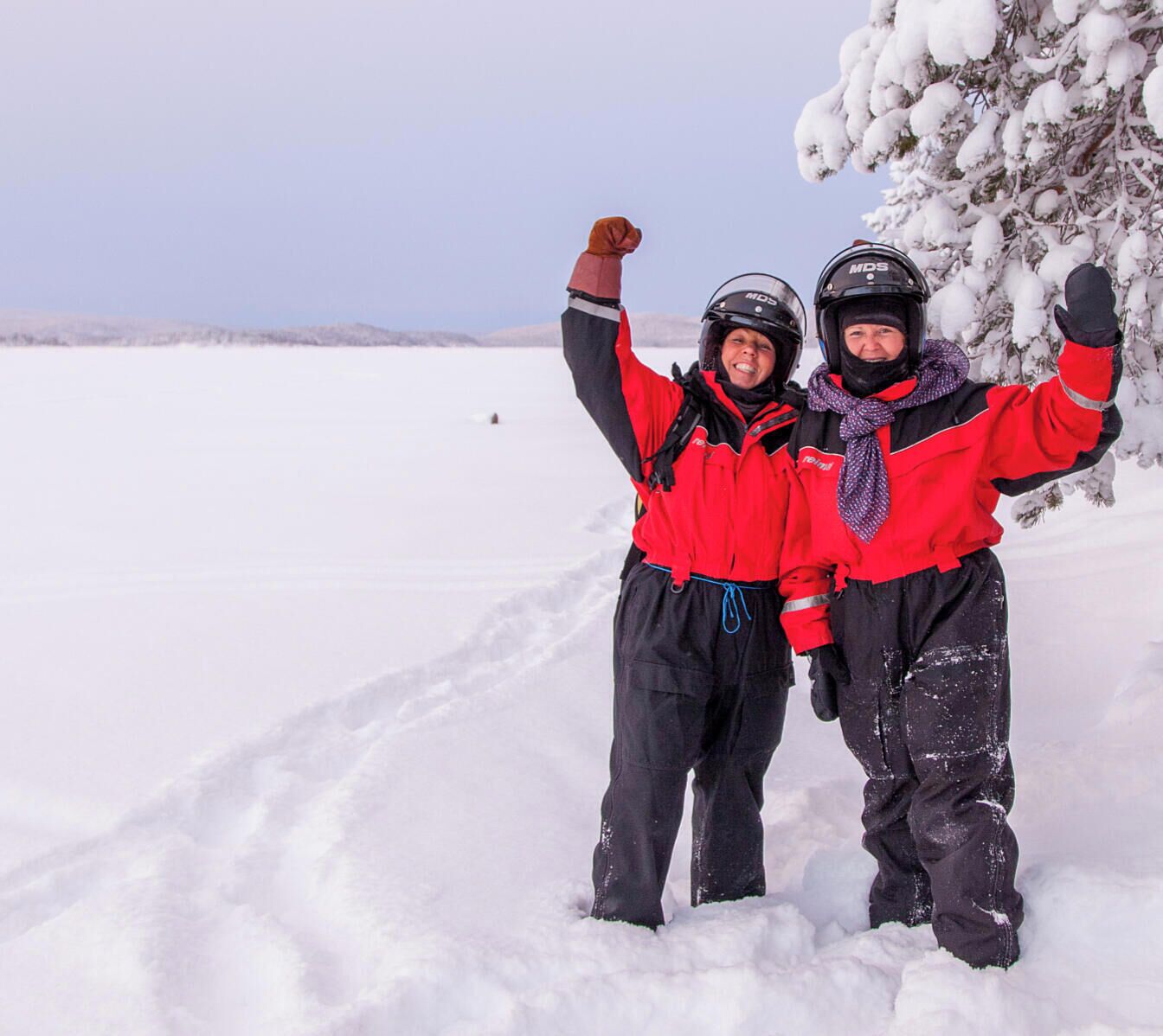 Two people in red and black winter gear standing in a snowy landscape.