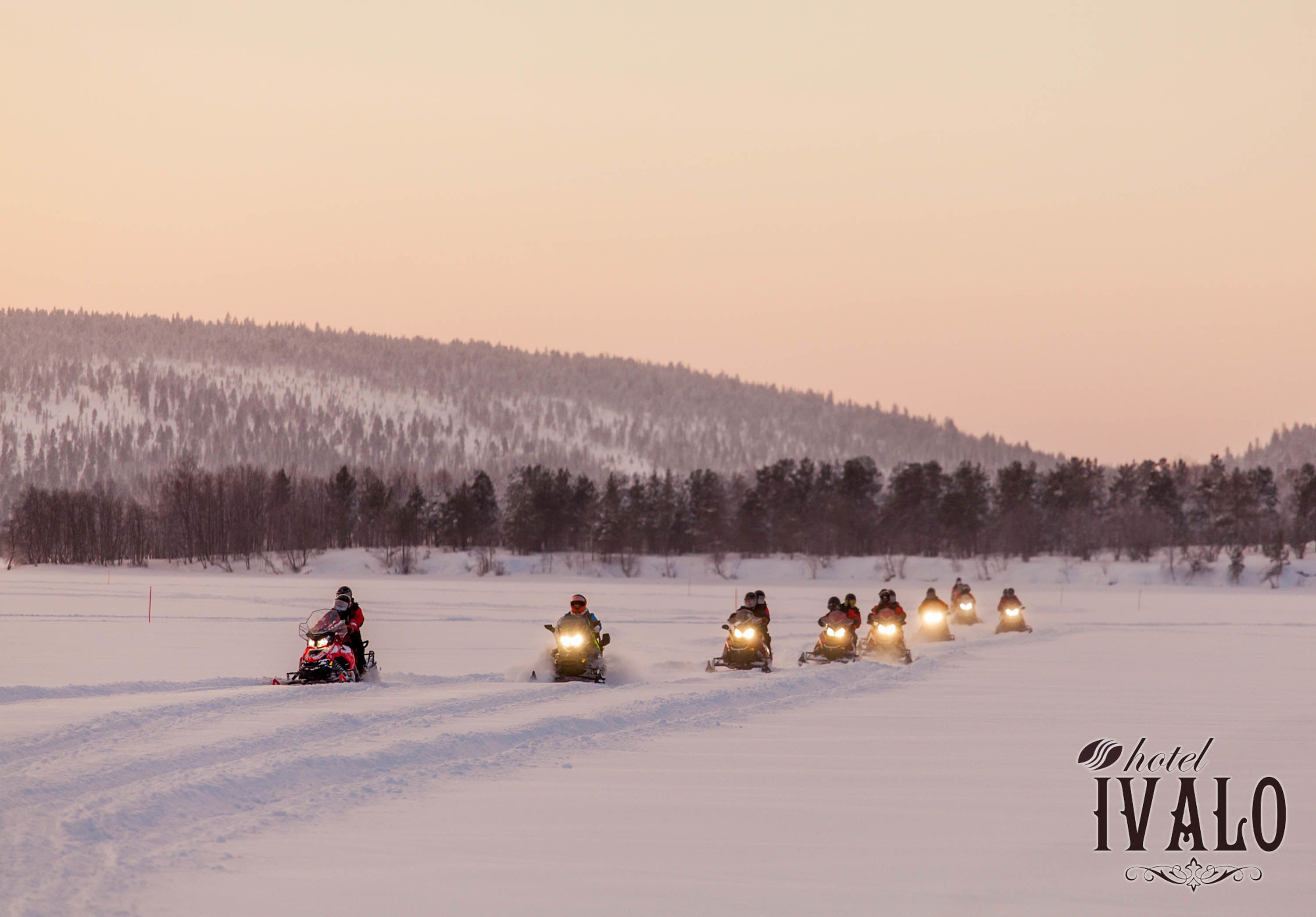 A group of snowmobiles on a snowy field with a forest in the background.
