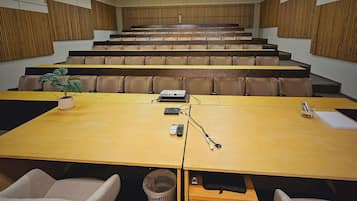 Un salón de conferencias con una larga mesa, sillas, un proyector y una planta.