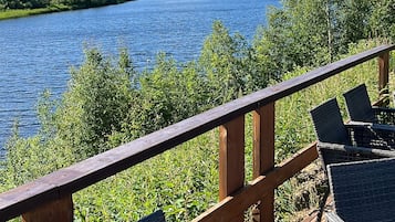 A deck with wicker chairs overlooking a lake, surrounded by greenery.