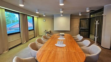 Une salle de conférence avec une table en bois, des chaises beiges, un écran de projection et une horloge au mur.