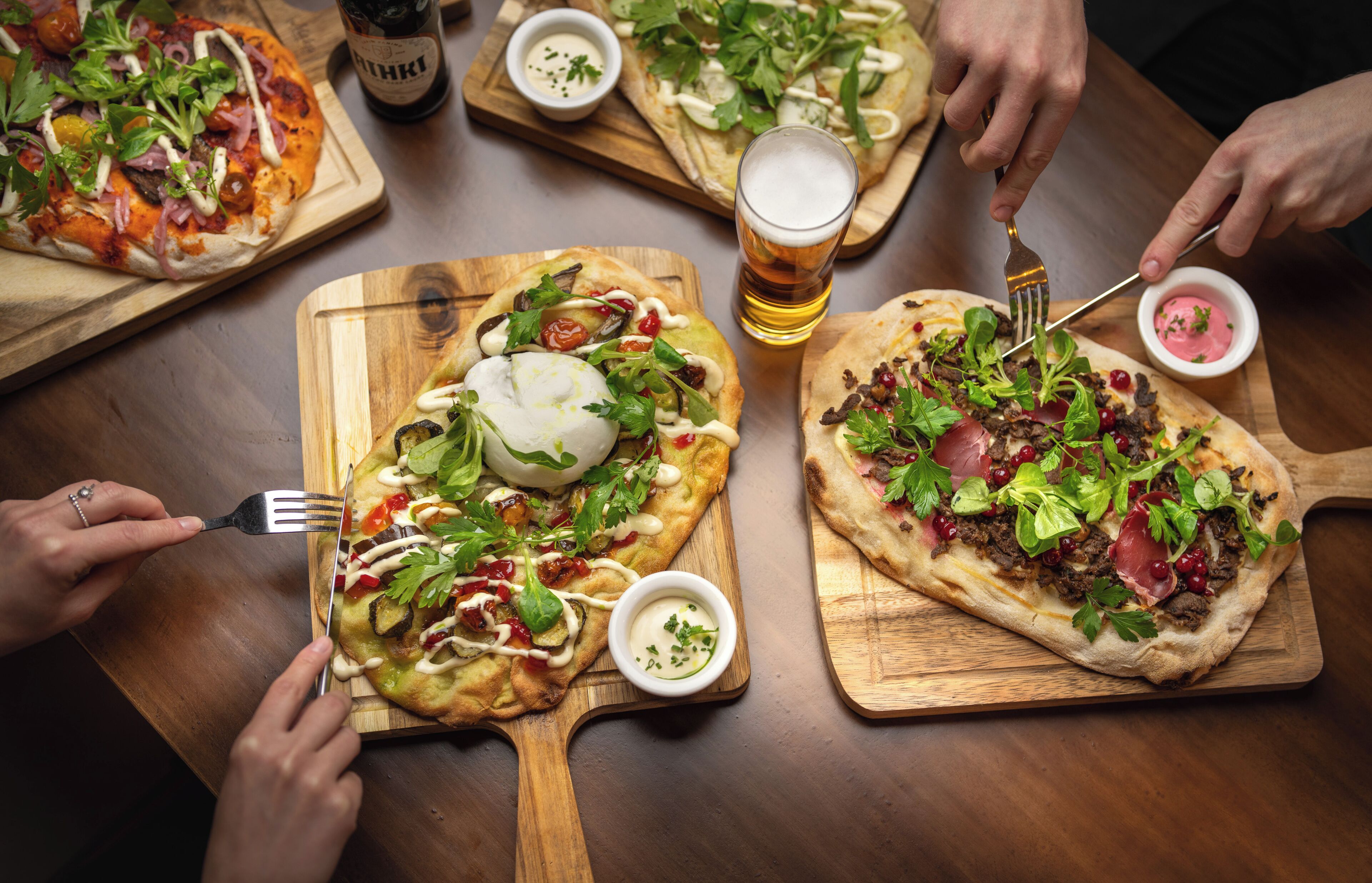 A dining table with three pizzas and a glass of beer.