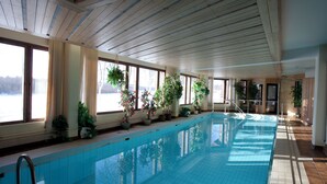 An indoor swimming pool with wooden beams, potted plants, and large windows. - Hotelli Ivalo (Inari)