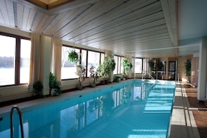 An indoor swimming pool with wooden beams, potted plants, and large windows. - Hotelli Ivalo (Inari)