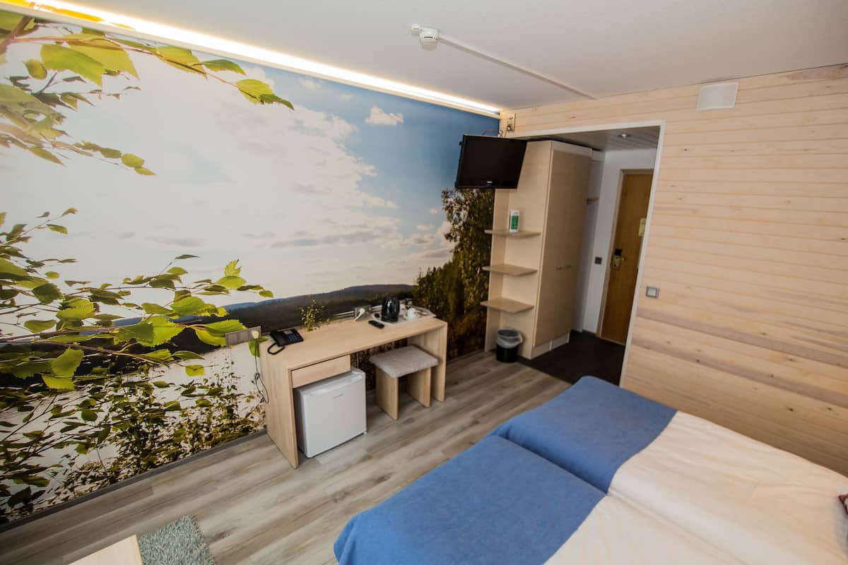 Quarto moderno com cama, escrivaninha e um pequeno frigorífico.