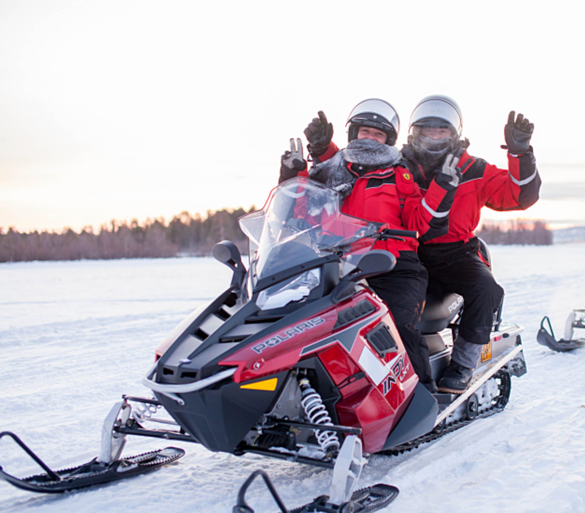 A snowmobile with two riders in red jackets and helmets.