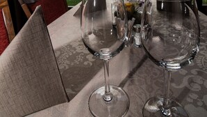 Una mesa preparada con copas de vino y una lámpara, con vistas a un jardín y árboles a través de una ventana.
