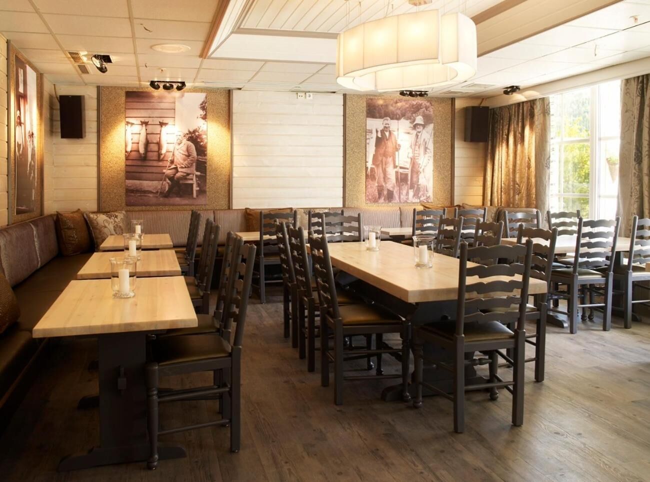 Ein Restaurant mit mehreren Holztischen und Stühlen, einem großen Kronleuchter und Vintage-Fotos an den Wänden.