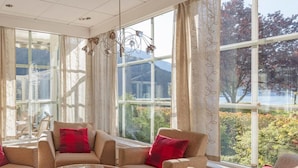 A room with a glass coffee table, beige sofas with red cushions, and large windows with a view of trees and mountains. - Loenfjord (Stryn)