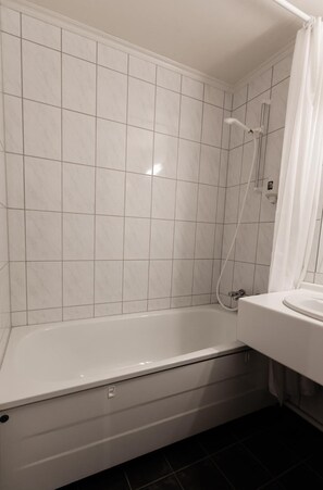A bathroom with a white bathtub, tiled walls, and a shower area.