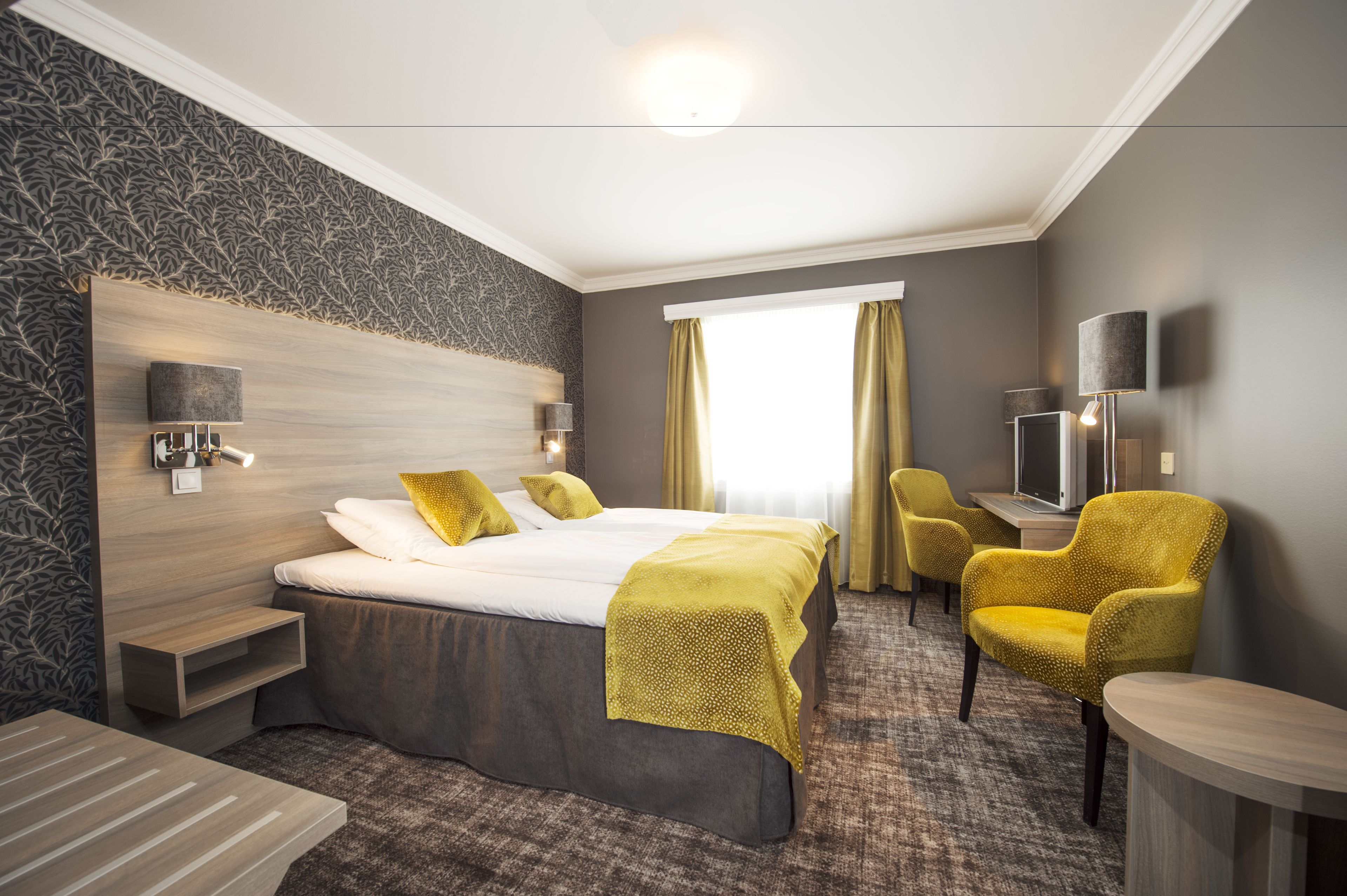 Habitación de hotel con una cama grande, un escritorio, una silla, un televisor y una ventana con cortinas.