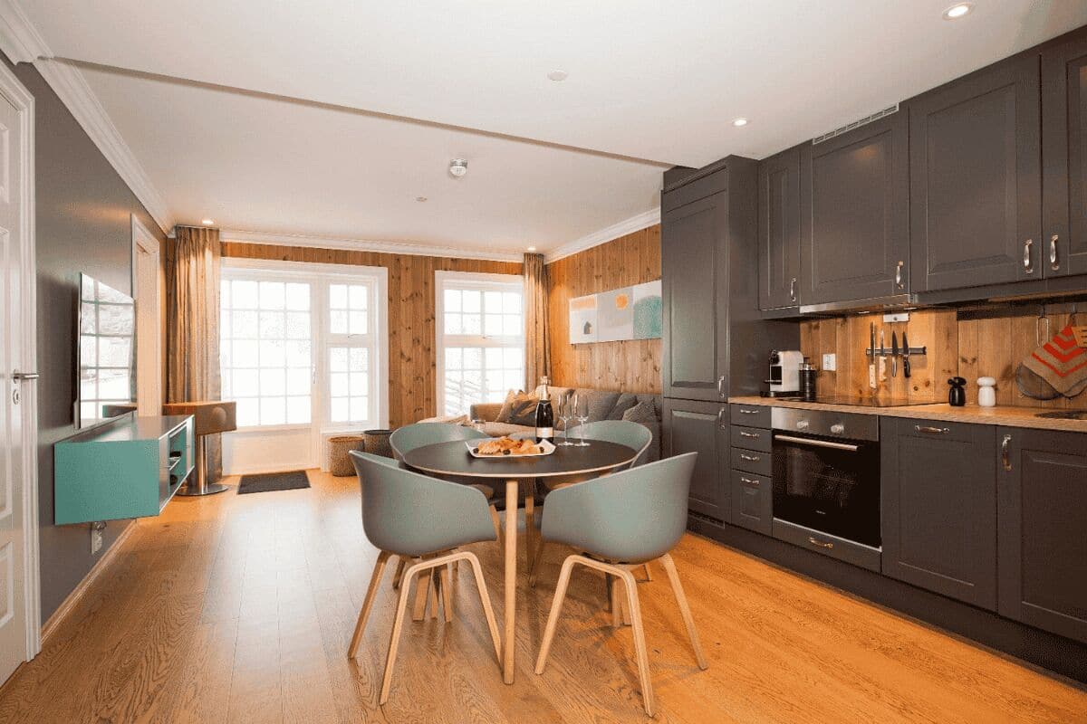 A modern kitchen with dark cabinets, a dining area with a round table and chairs, and a wooden floor.