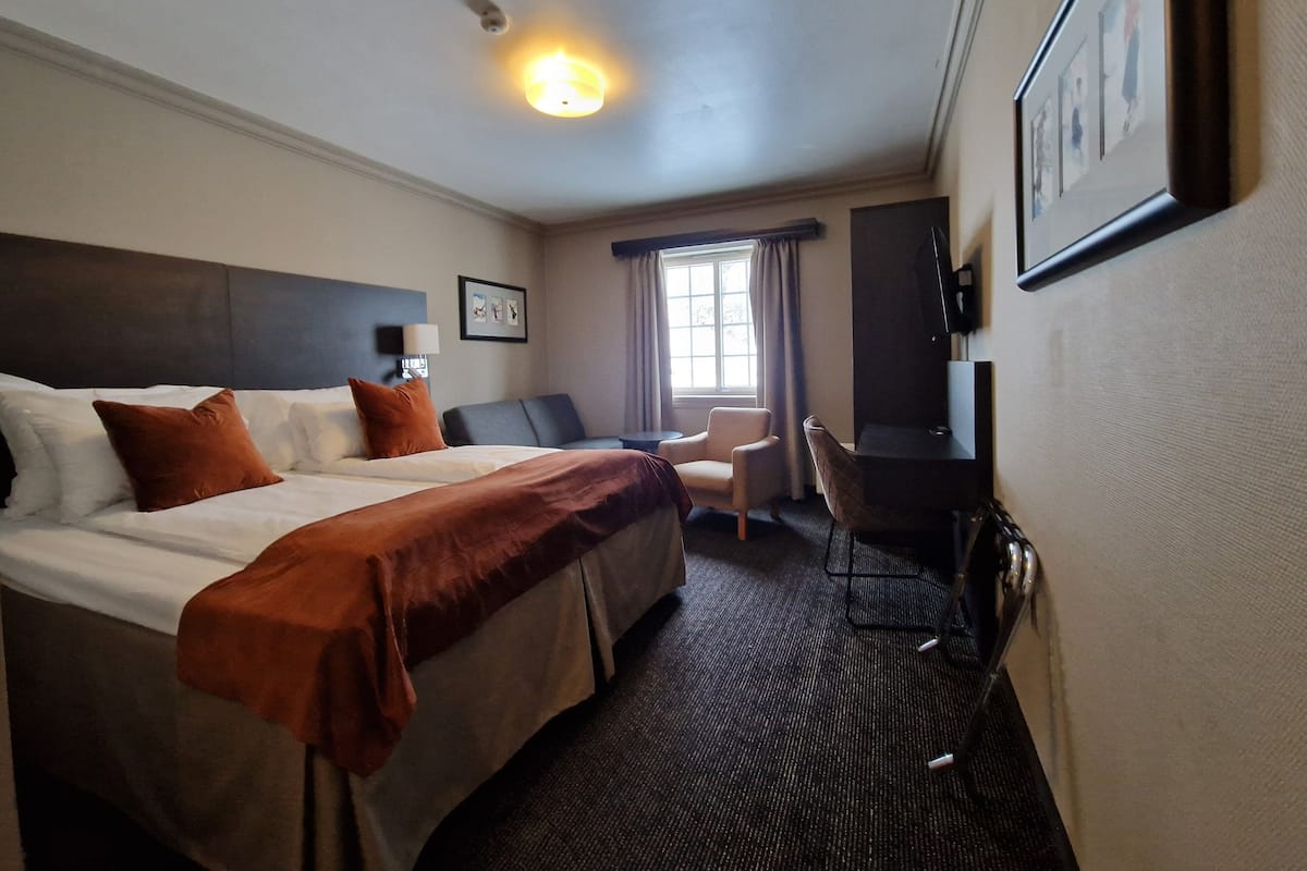A hotel room with a large bed, a desk, a chair, a TV, and a window with curtains.