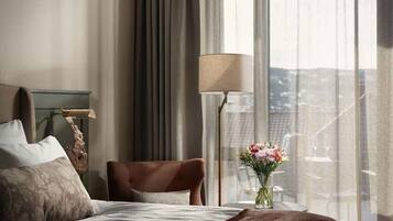A hotel room with a bed, a chair, a lamp, and a view of the city through large windows.