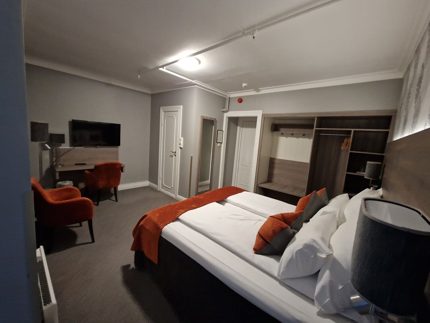 Una habitación de hotel con una cama, un escritorio, una silla, un televisor y un armario.