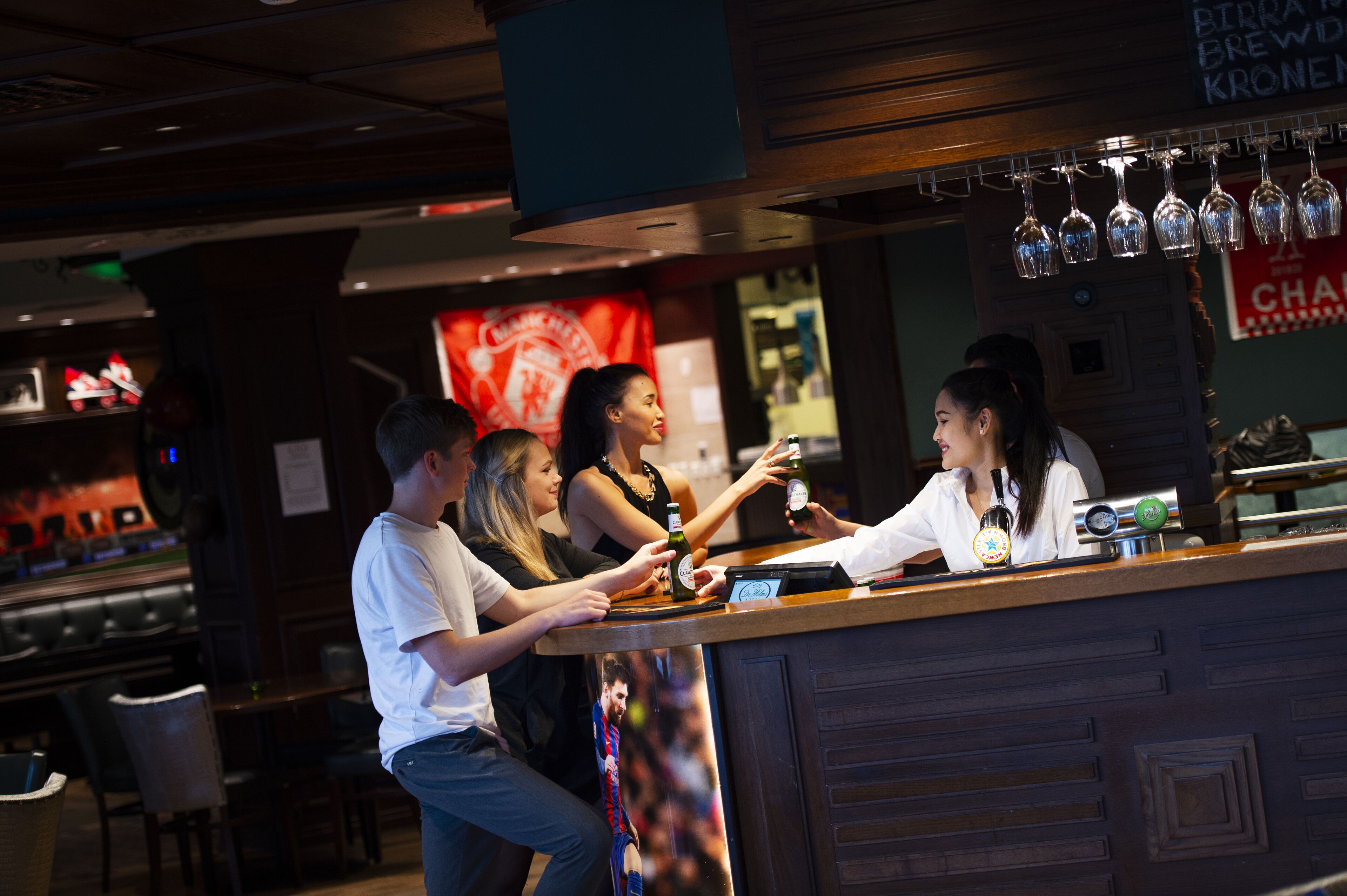 Un espace bar avec un comptoir, des verres suspendus au-dessus et un tableau affichant le menu.