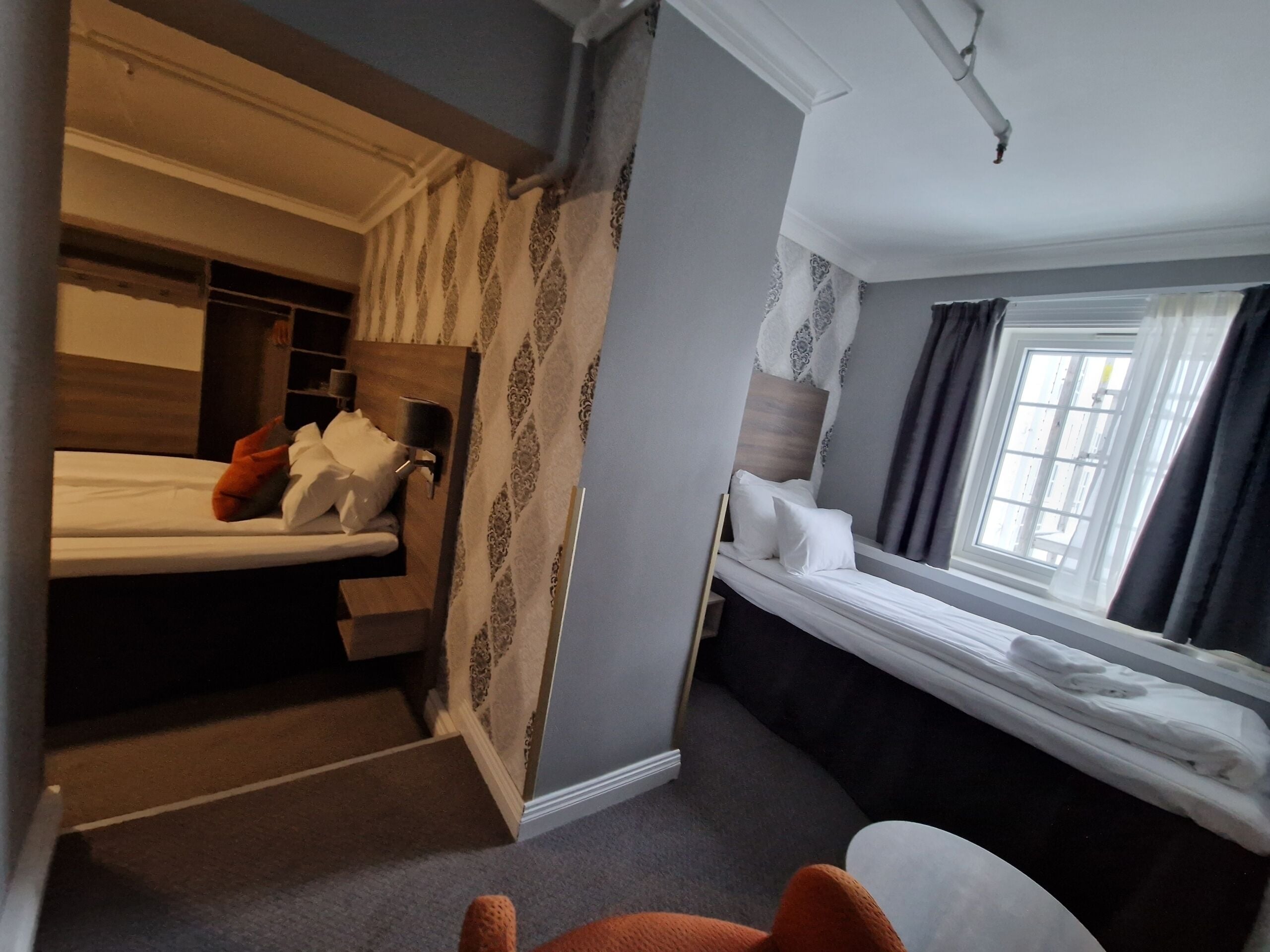 Ein Hotelzimmer mit Etagenbett, Schreibtisch mit Stuhl, Fenster mit Vorhängen und einem kleinen Tisch.