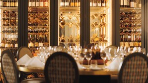 A restaurant with a long table set for dining, surrounded by wine racks filled with bottles. - Dr. Holms Hotel (Hol)