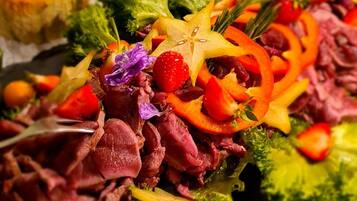 A buffet with various dishes including meat, vegetables, and fruits.