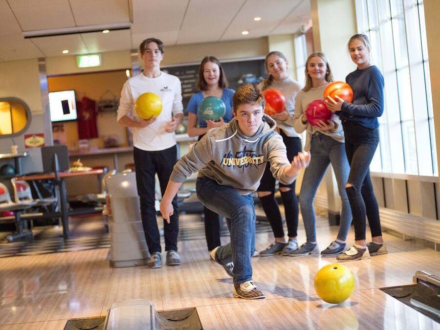 Una bolera con piso de madera y un grupo de personas jugando a los bolos.