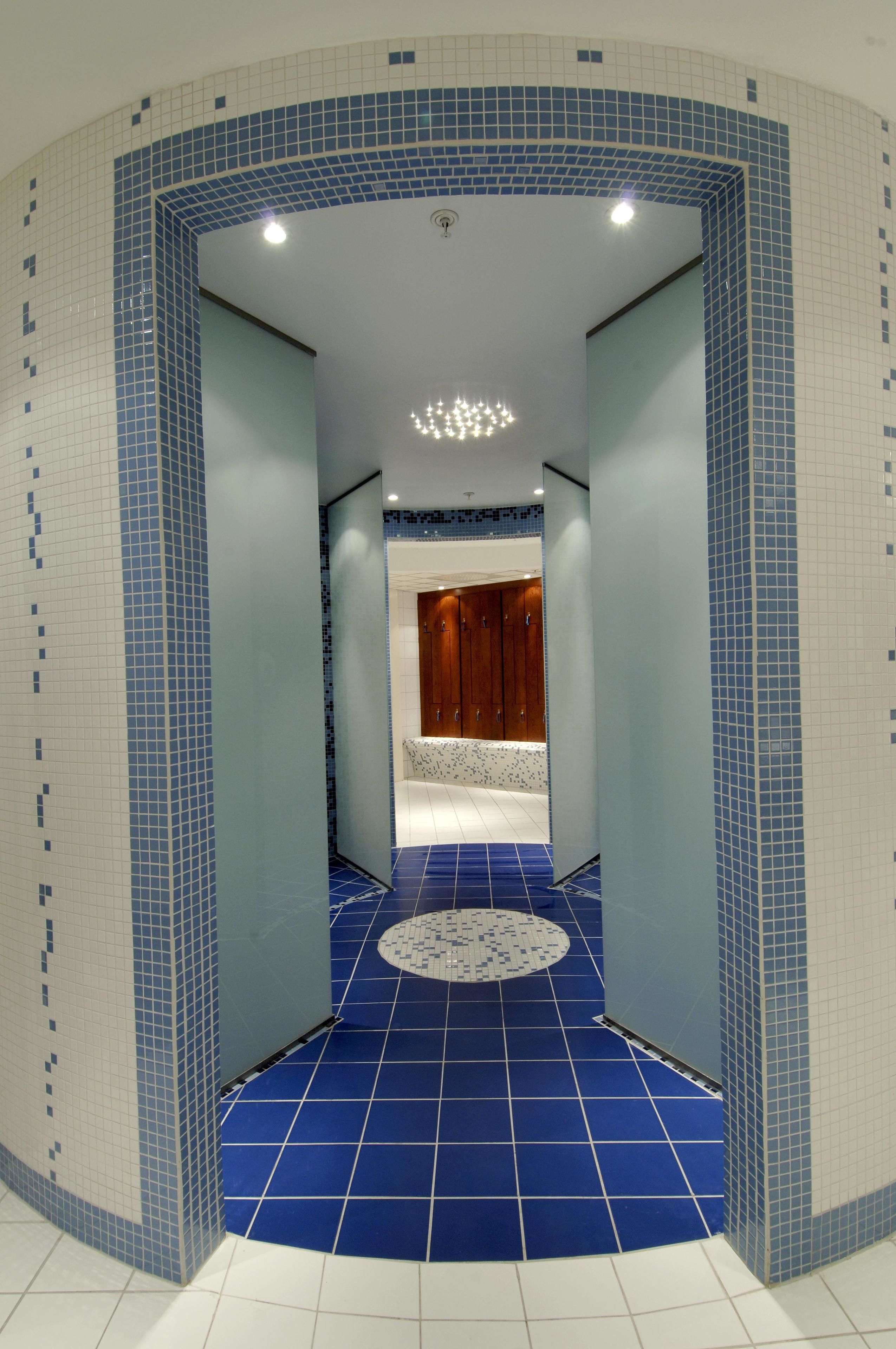 A hallway with blue-tiled flooring, a circular patterned area, and wooden doors leading to a room.