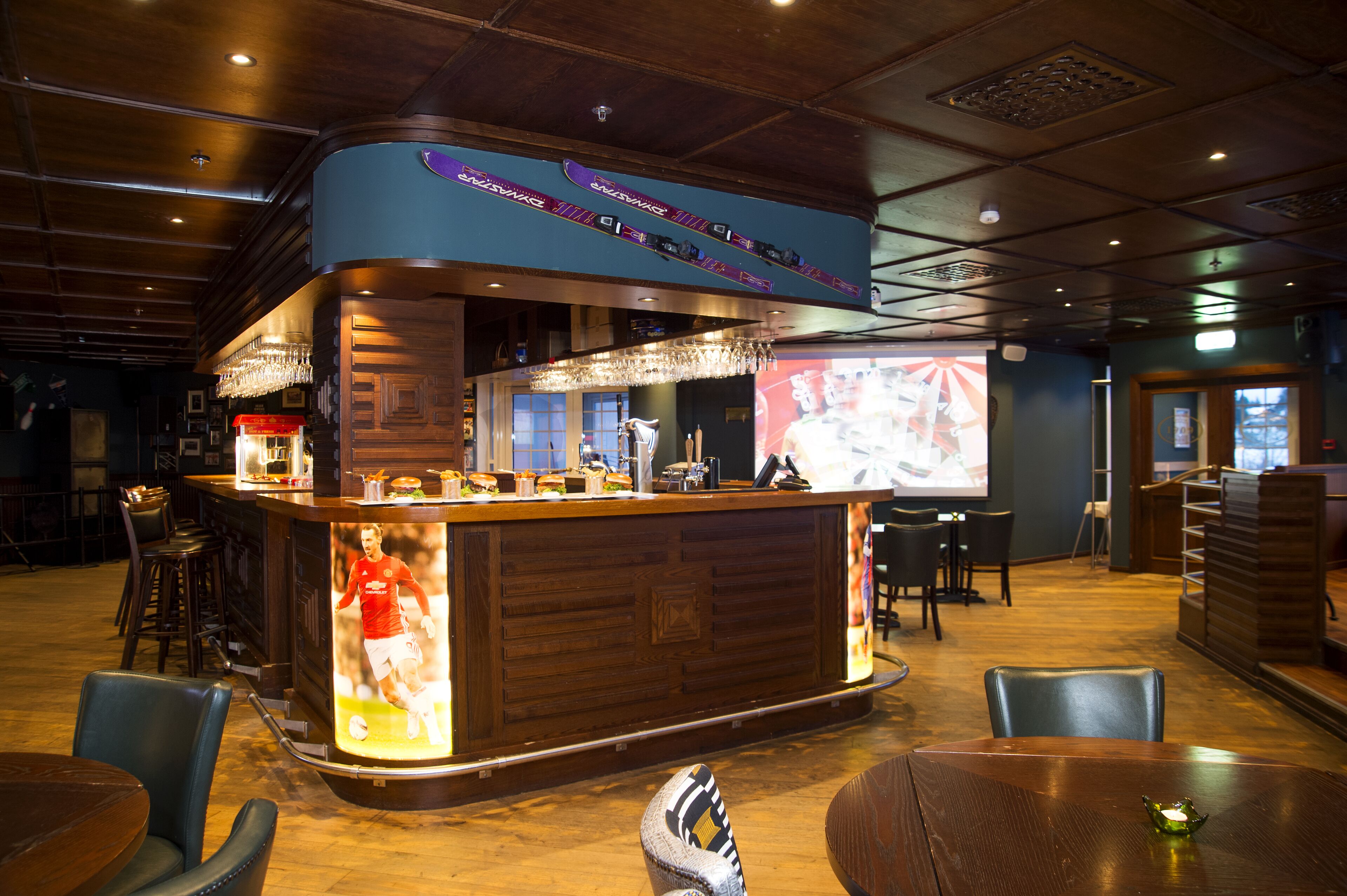 A bar area with a counter, stools, and a screen displaying a sports event.