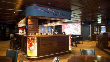 A bar area with a counter, stools, and a screen displaying a sports event.