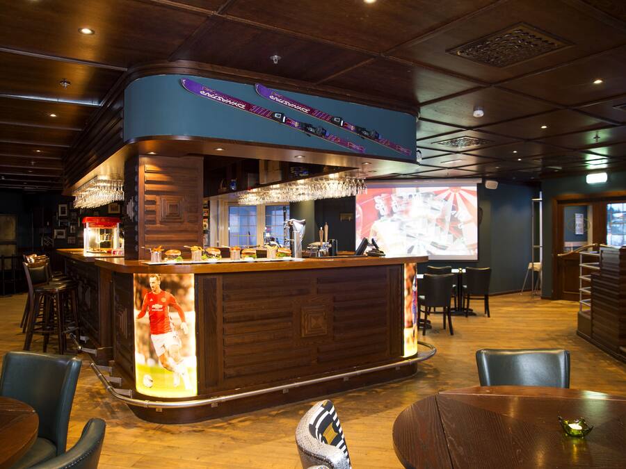 A bar area with a counter, stools, and a screen displaying a sports event.