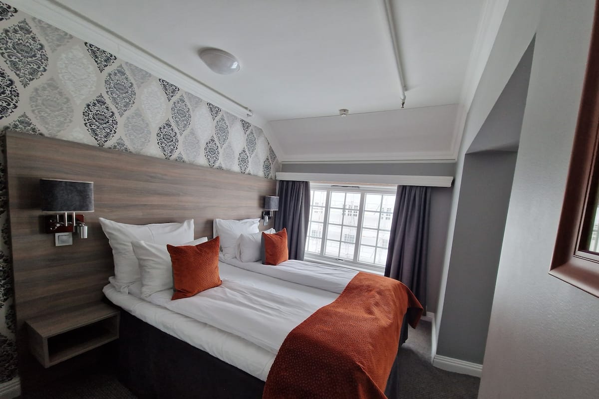A hotel room with a large bed, a bedside table with a lamp, and a window with curtains.