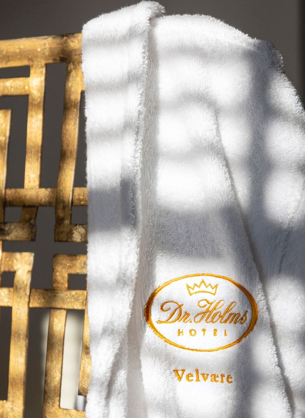 A white towel with embroidered text "Dr. Holms Hotel" and "Velvure" on a wooden chair.