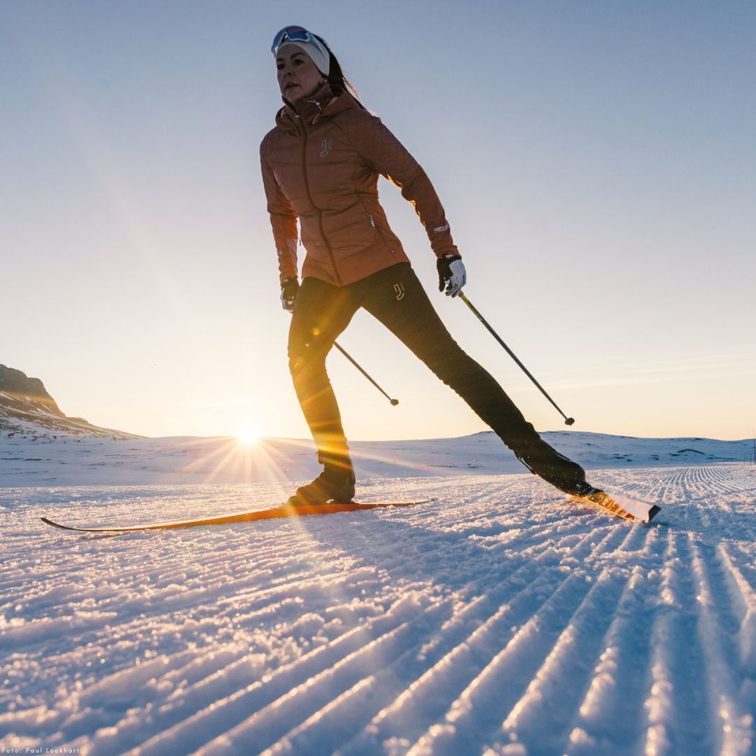 Una persona esquiando en una pendiente nevada con el sol poniéndose en el horizonte.