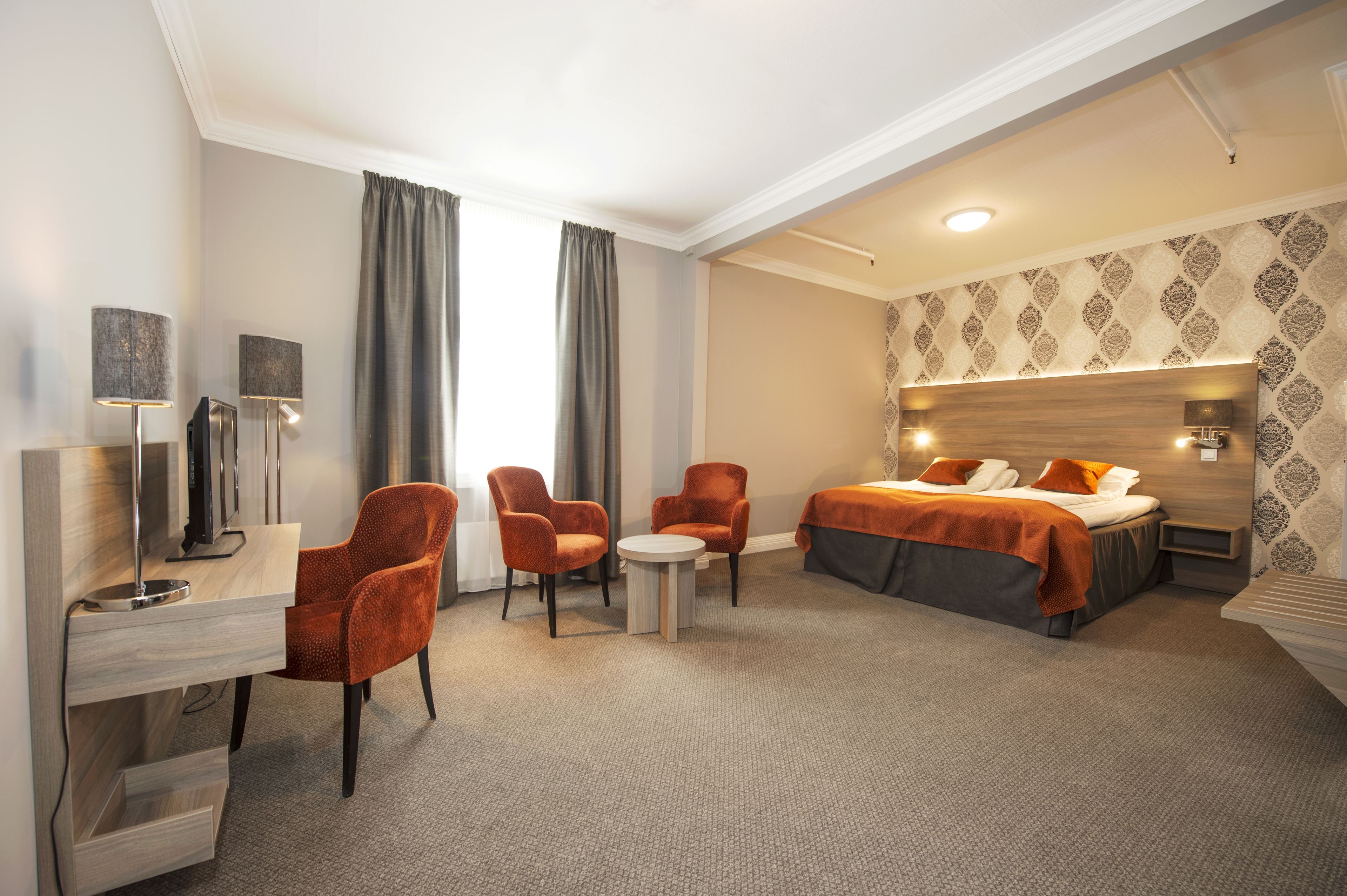 A hotel room with a bed, two armchairs, a desk with a lamp, and a small table.