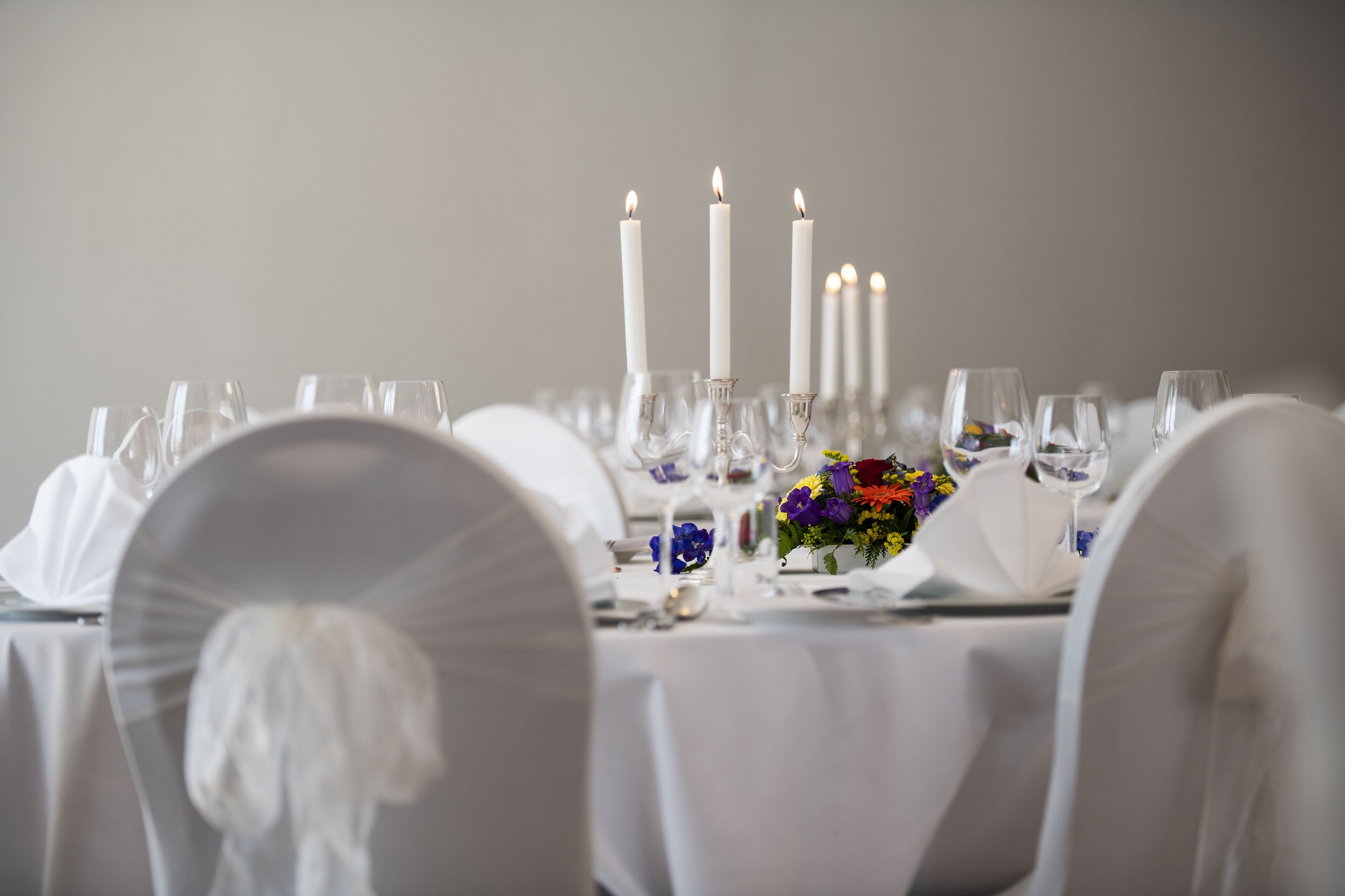 A table set with white tablecloths, candles, and a floral centerpiece.