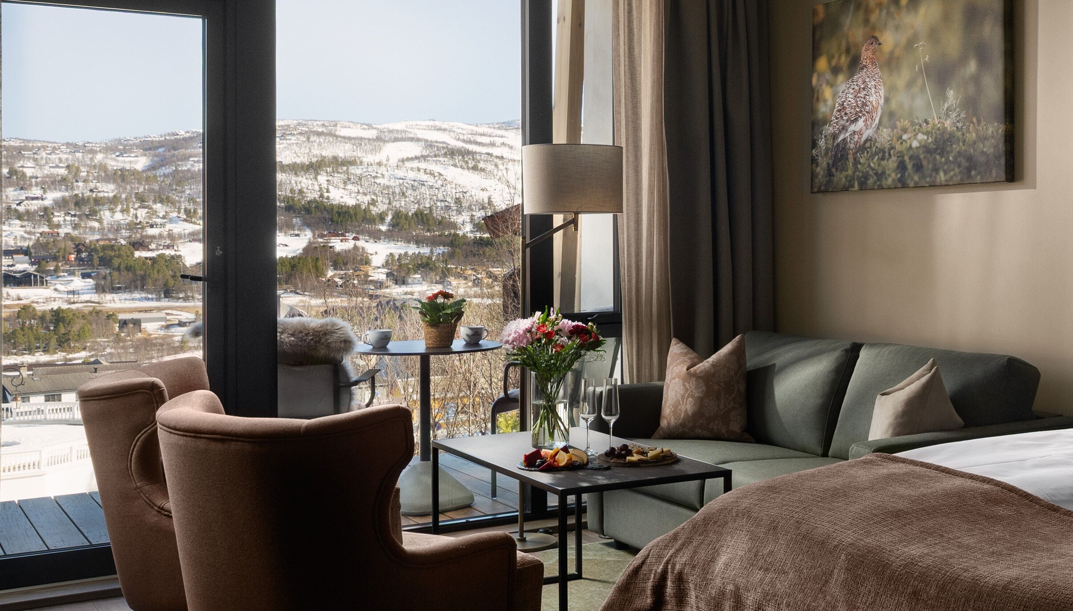Una habitación de hotel con sofá, una mesa con flores, una lámpara y un cuadro.