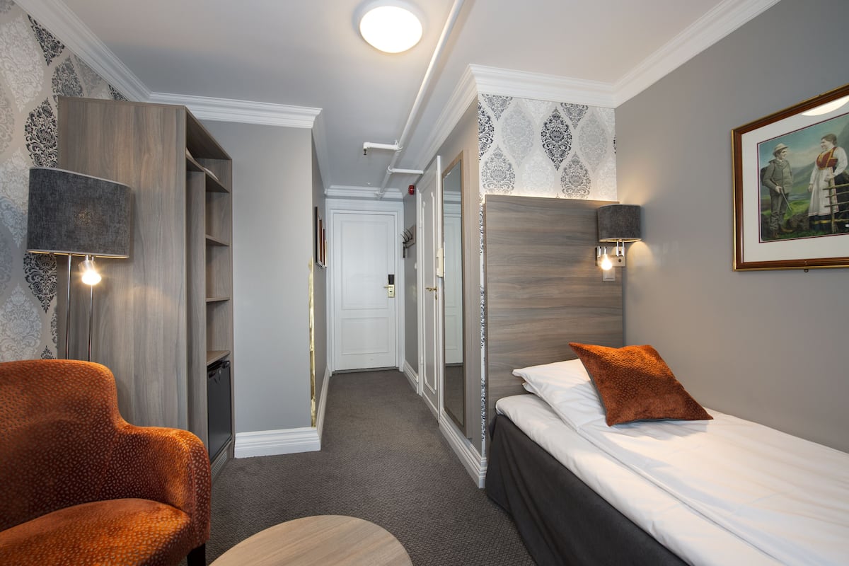 A hotel room with a bed, a chair, a desk, and a wardrobe.